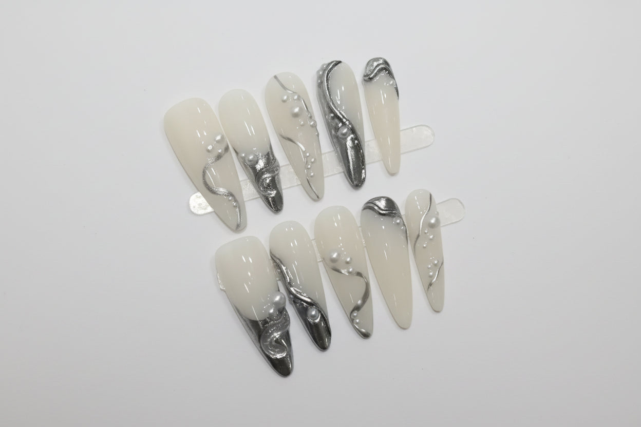 Set of decorative false nails with silver and gold accents on a white card.